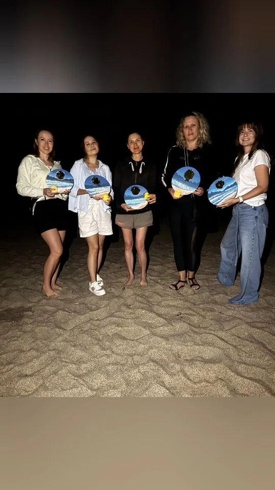 Guests holding finished paintings after an ocean-side workshop